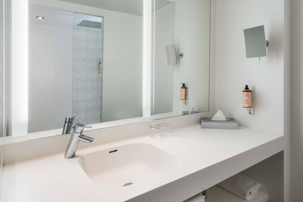 A modern bathroom with a large mirror, a white sink, and two wall-mounted soap dispensers.