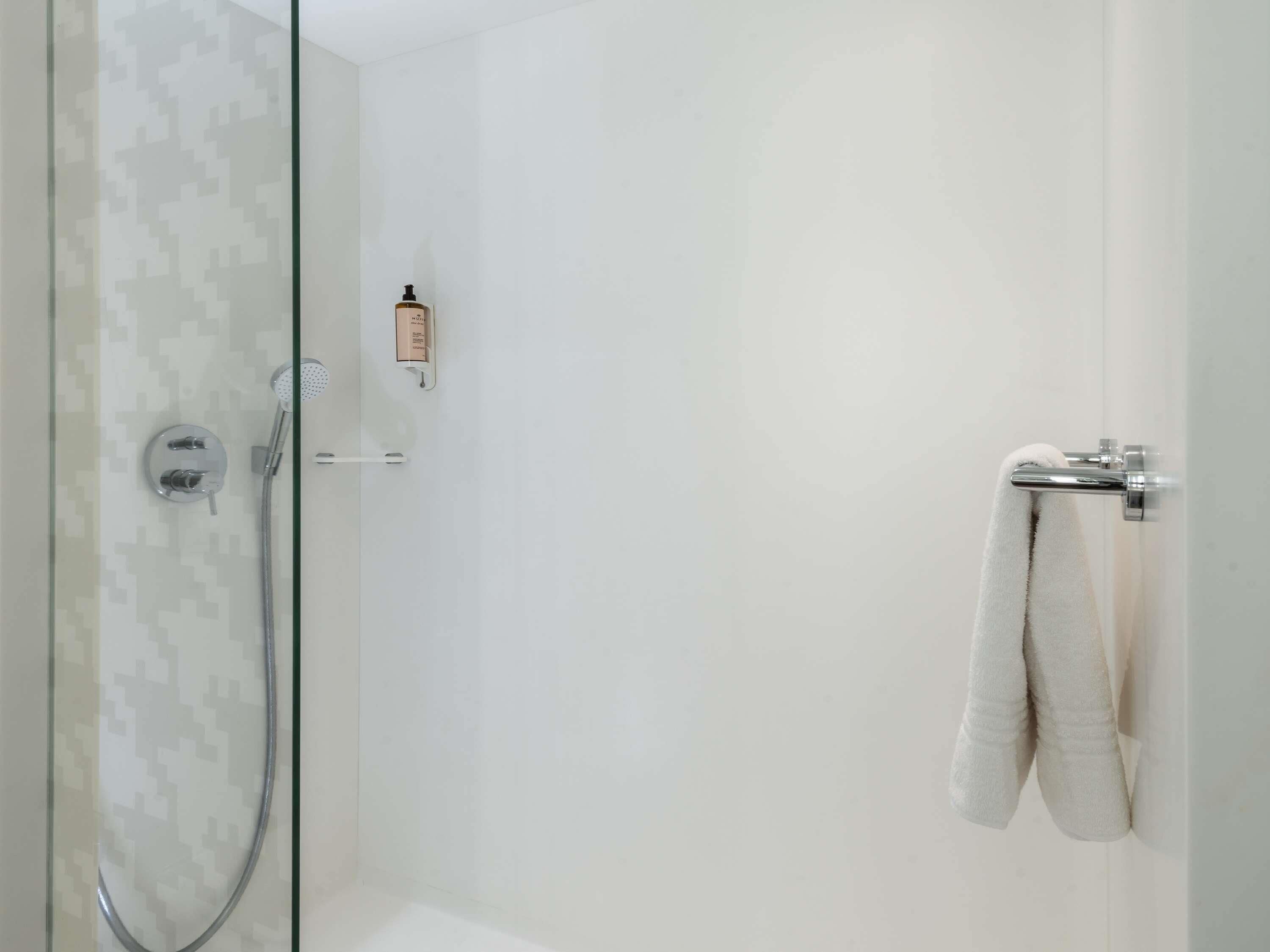 A modern shower area with a glass door, a handheld showerhead, and a towel rack with a towel hanging on it.