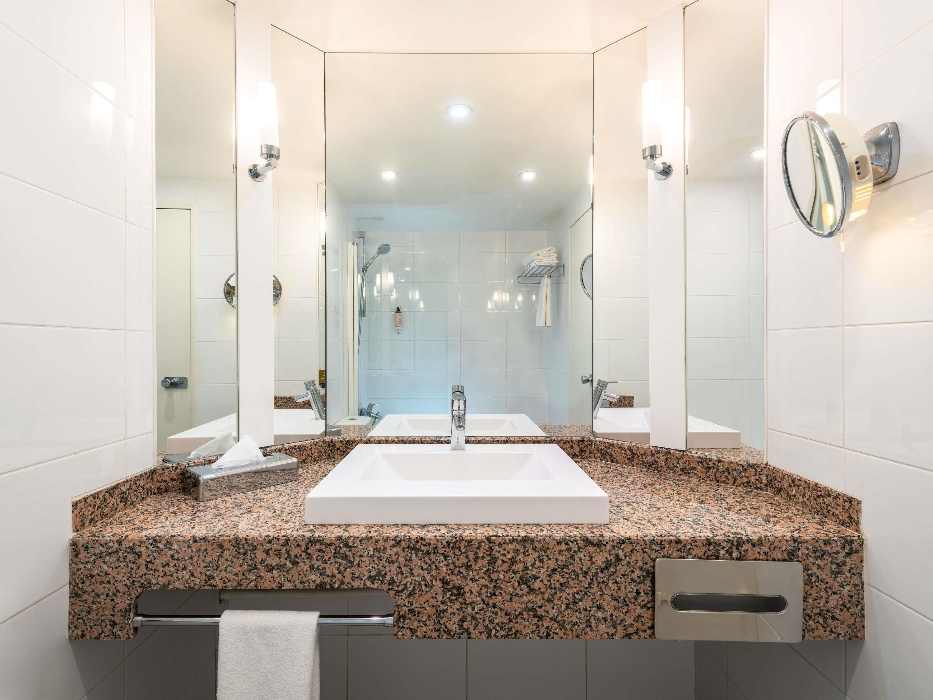 A modern bathroom with a large sink, two mirrors, and a shower area.