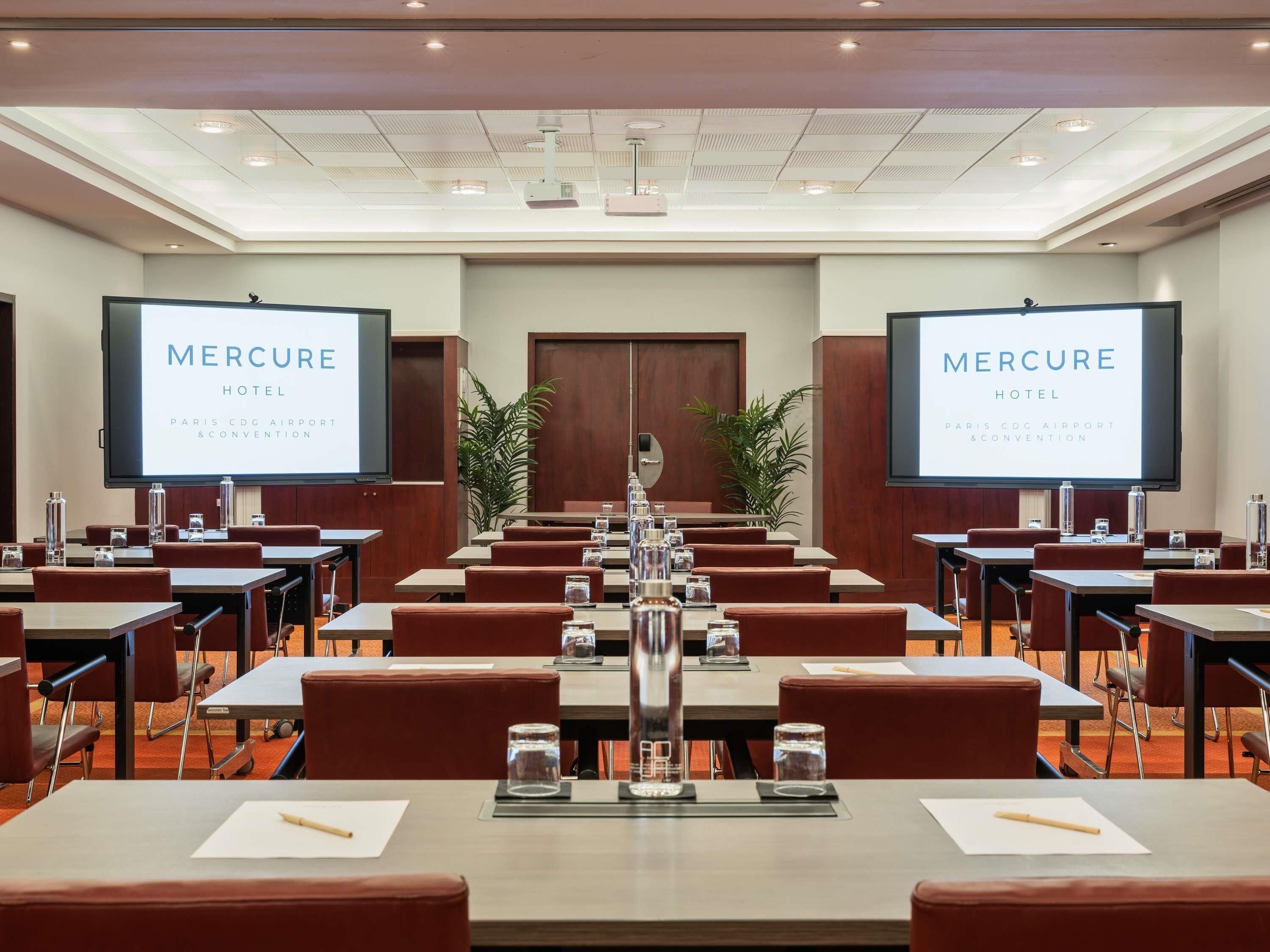 A conference room with tables, chairs, and a large screen displaying 'Mercure Hotel Paris CDG Airport & Convention'.