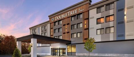 Un hôtel DoubleTree by Hilton doté d’une façade moderne, d’une entrée abritée et d’un espace paysager agrémenté d’un petit arbre.