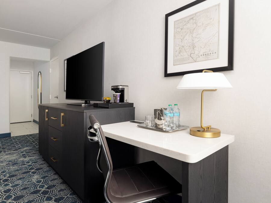A hotel room with a desk, a chair, a television, a map on the wall, and a coffee machine.