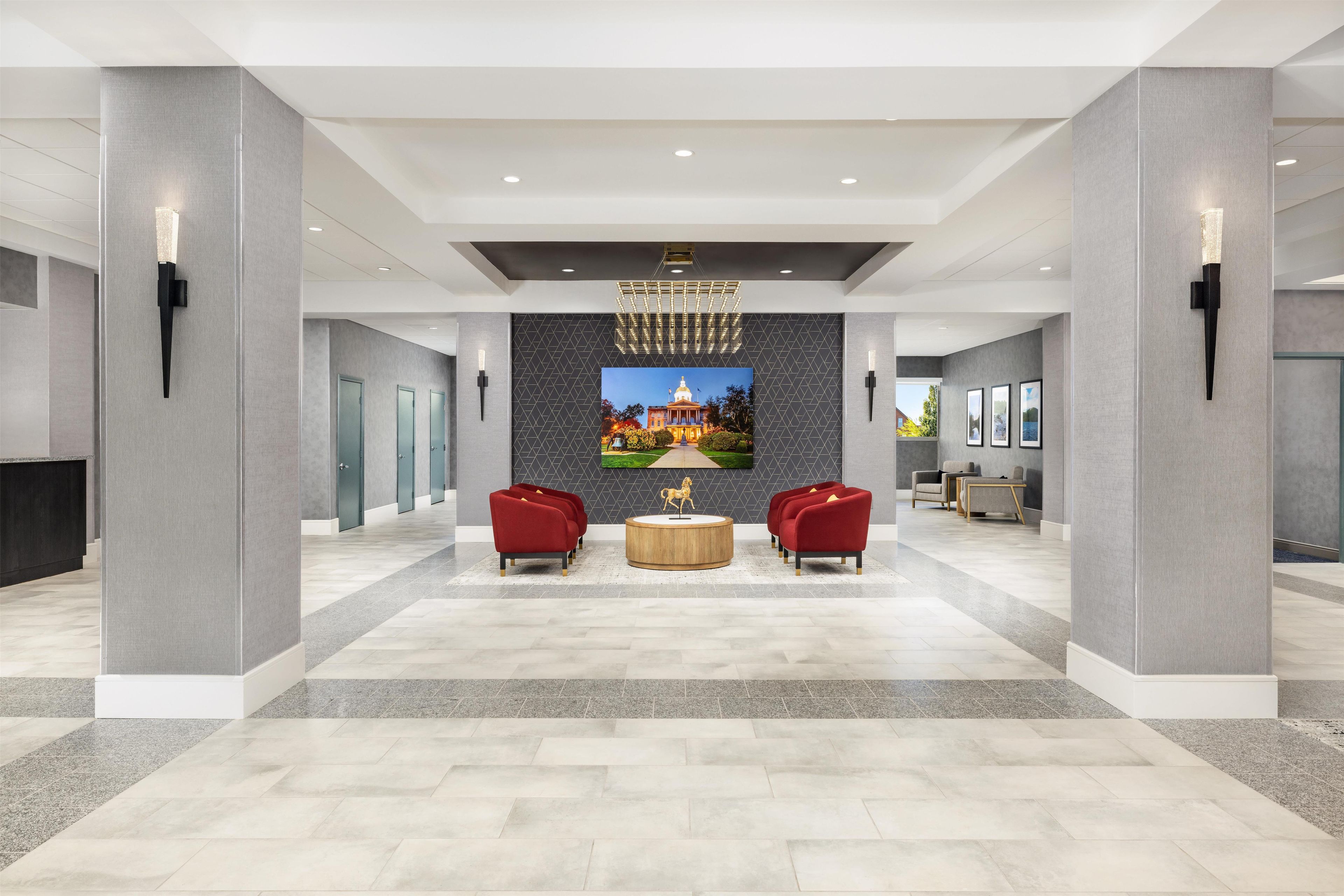 A spacious lobby with a modern chandelier, a large wall mural, and seating areas.