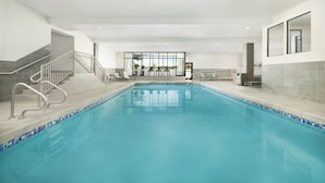 A large indoor swimming pool with a tiled edge, a staircase with metal railings, and a seating area with tables and chairs. - DoubleTree by Hilton Downtown Concord (Concord)