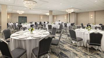 A banquet hall with round tables set for dining, featuring white tablecloths, dark chairs, and chandeliers.