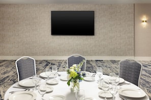A conference room with a round table set for a meeting, a flat-screen TV mounted on the wall, and a decorative vase with flowers. - DoubleTree by Hilton Downtown Concord (Concord)