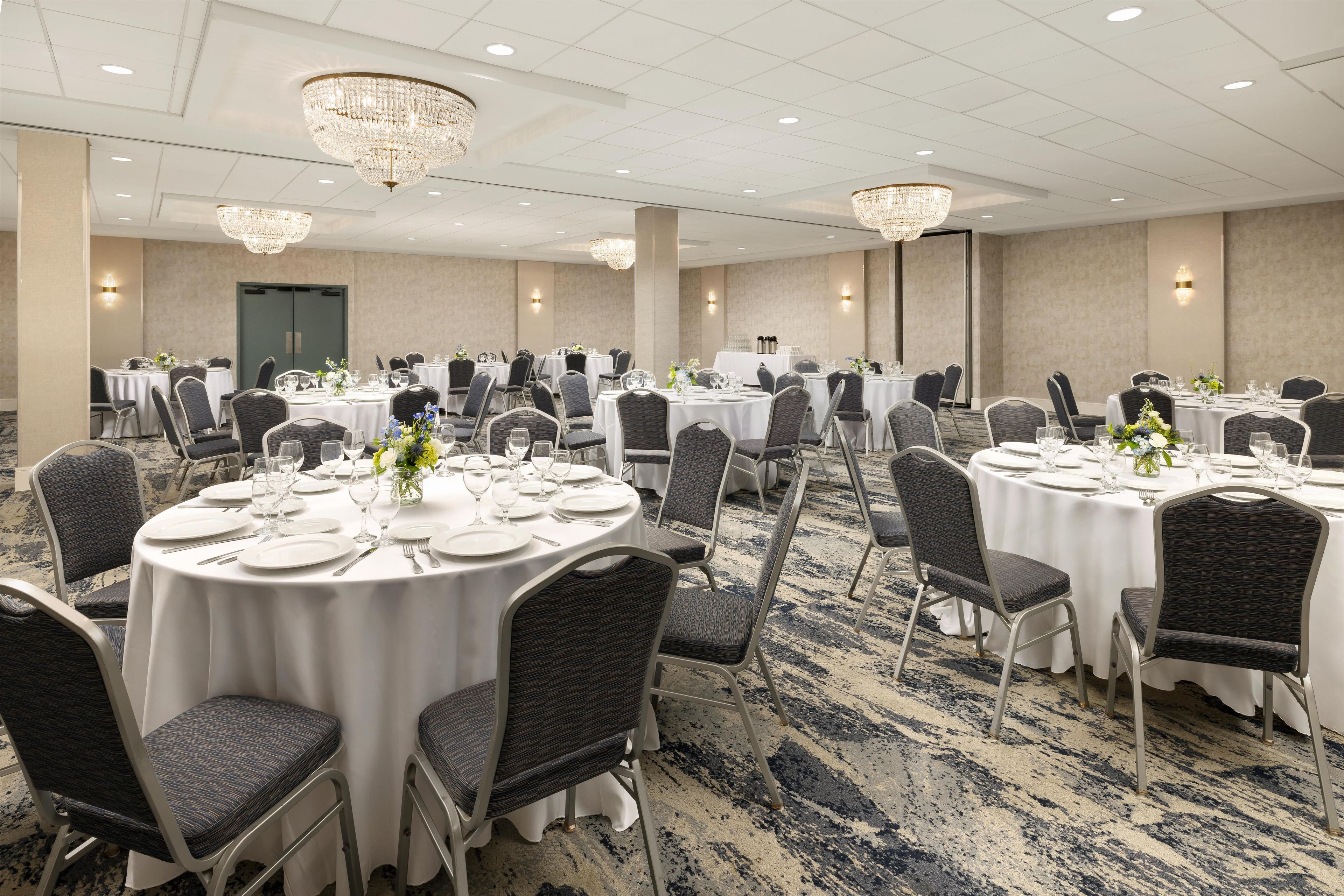 A banquet hall with round tables, chairs, and chandeliers.