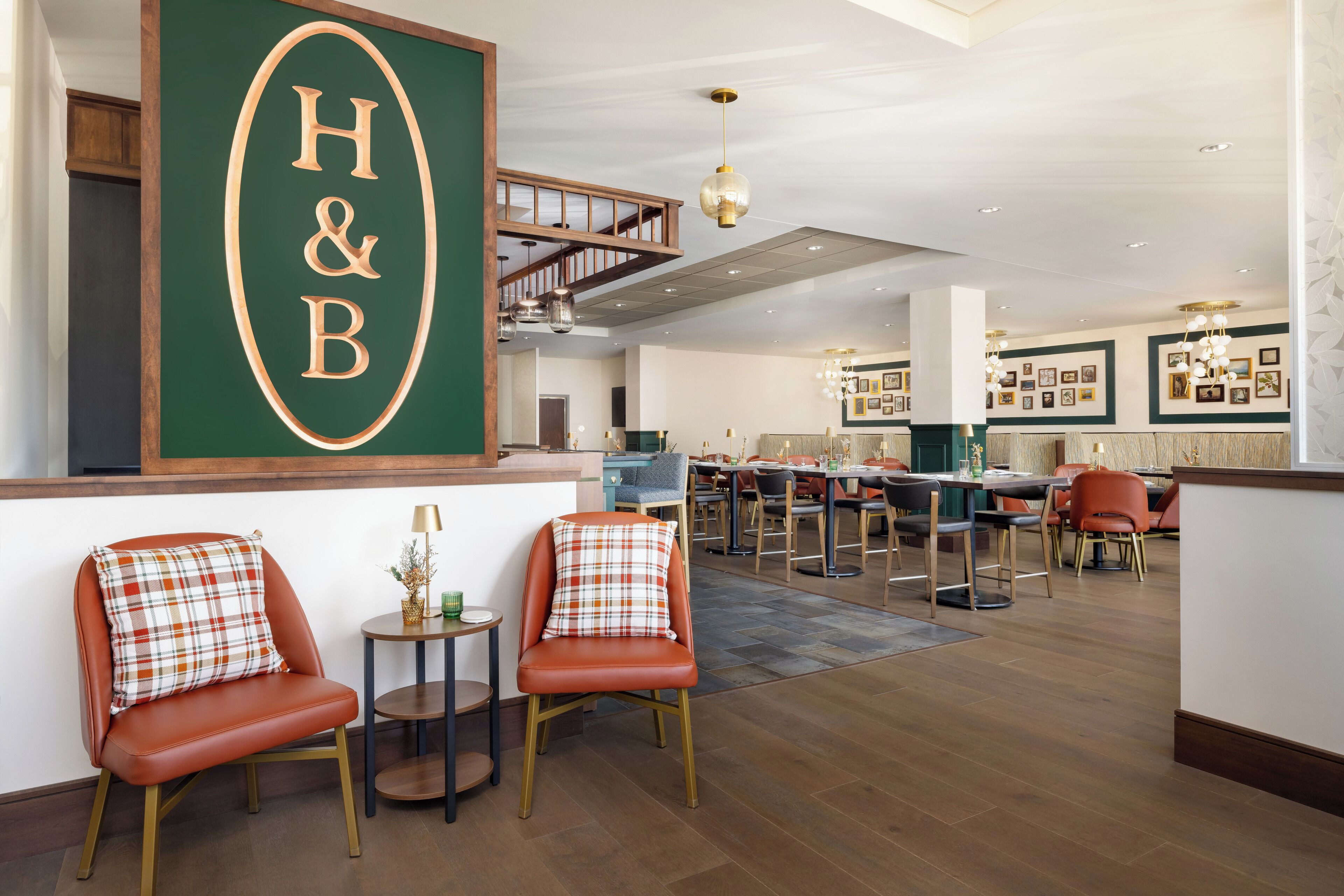 A spacious hotel lobby with a prominent H&B sign, comfortable seating, and a staircase leading to upper floors.