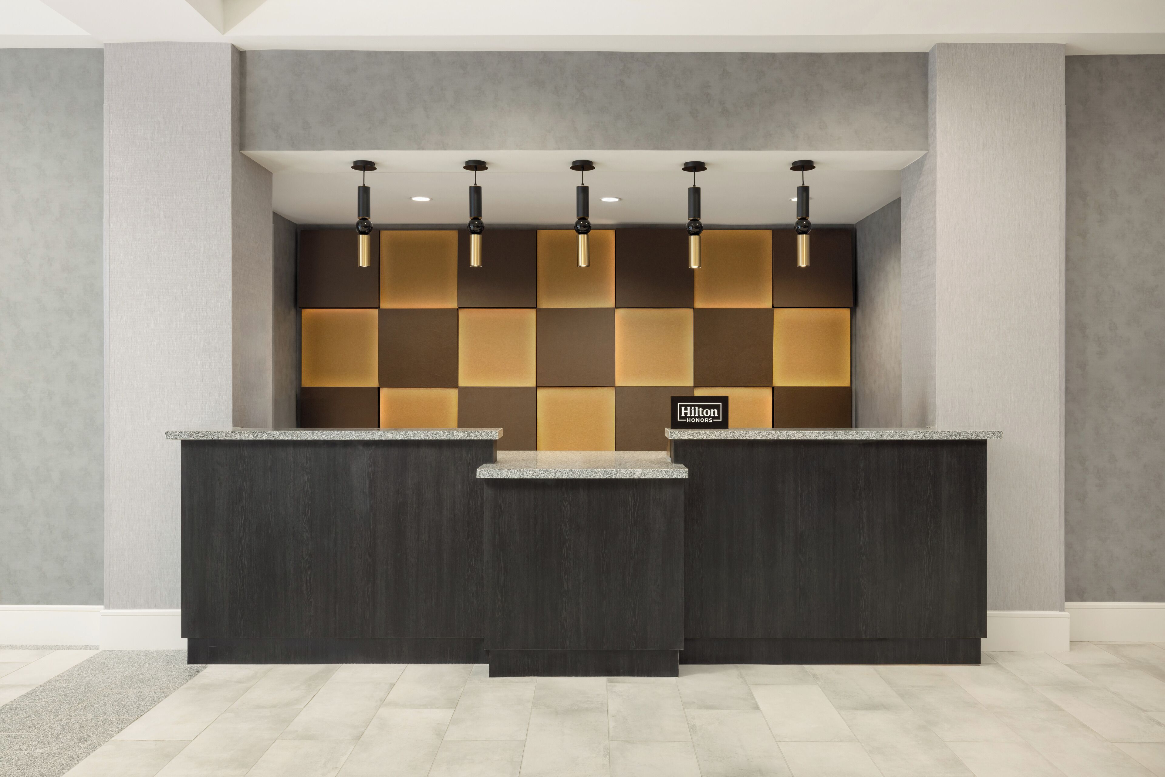 A reception desk with a check-in counter, a wall with a geometric pattern, and a logo on the wall.
