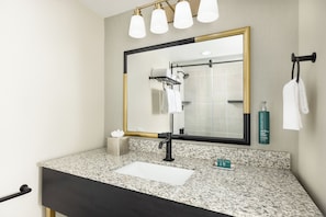 A bathroom with a granite countertop, a black sink, a mirror with a gold frame, and a shower visible in the reflection. - DoubleTree by Hilton Downtown Concord (Concord)