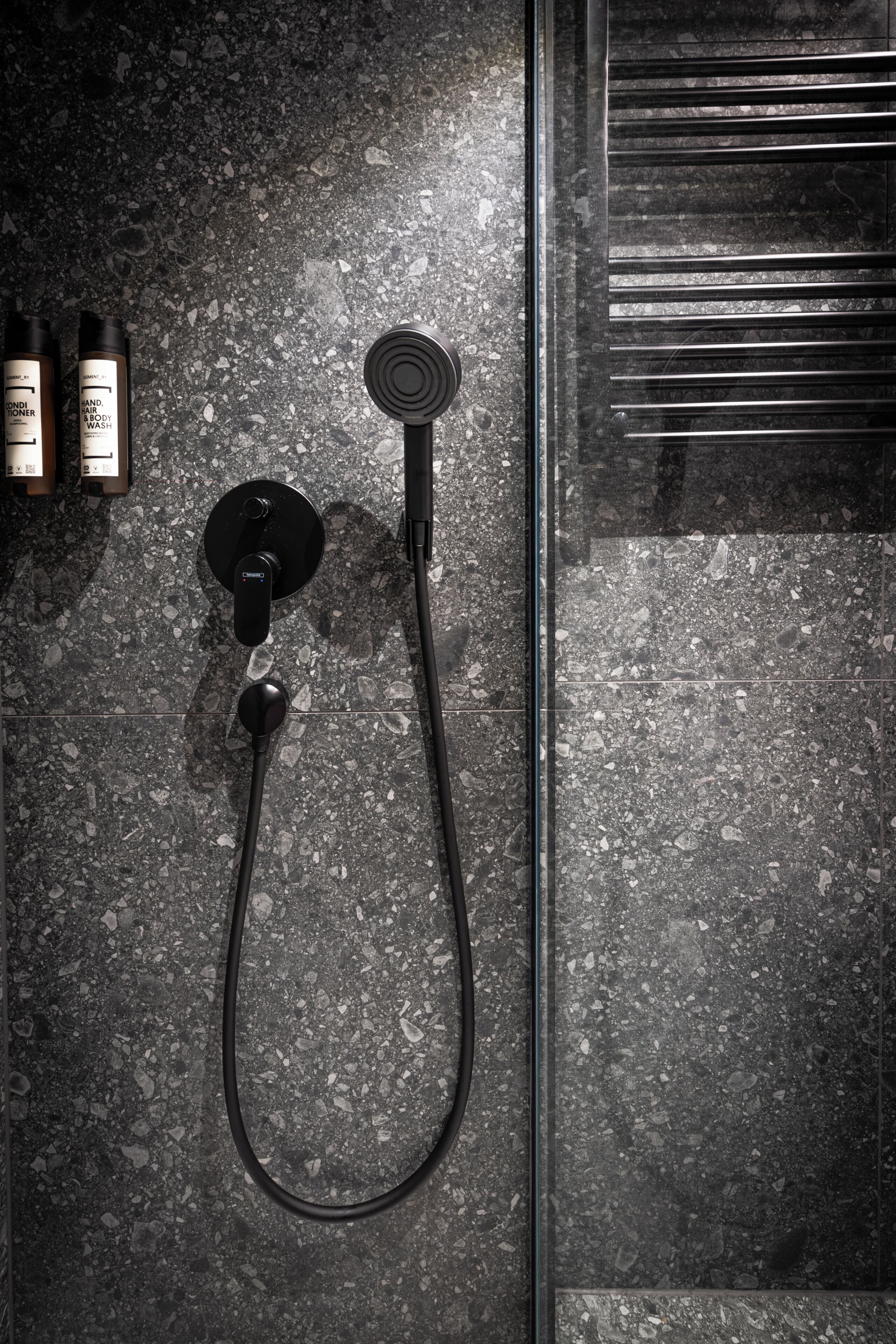 A shower with a handheld attachment, a wall-mounted control, and a glass door.