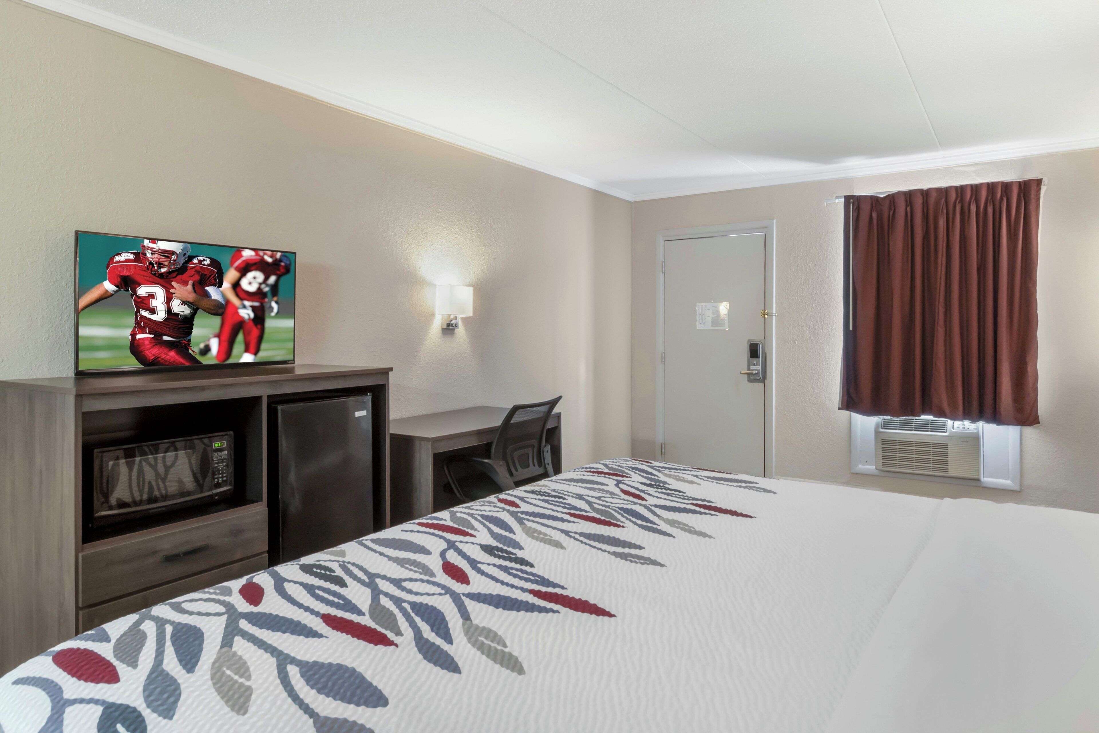 Una habitación de hotel con una cama, un escritorio, un televisor, un microondas y una puerta.