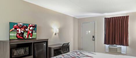 Una habitación de hotel con una cama, un escritorio, un televisor, un microondas y una puerta.
