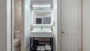 A narrow bathroom with a white sink, a mirror above it, and a black shelf below. - Red Roof Inn Manchester, TN (Manchester)