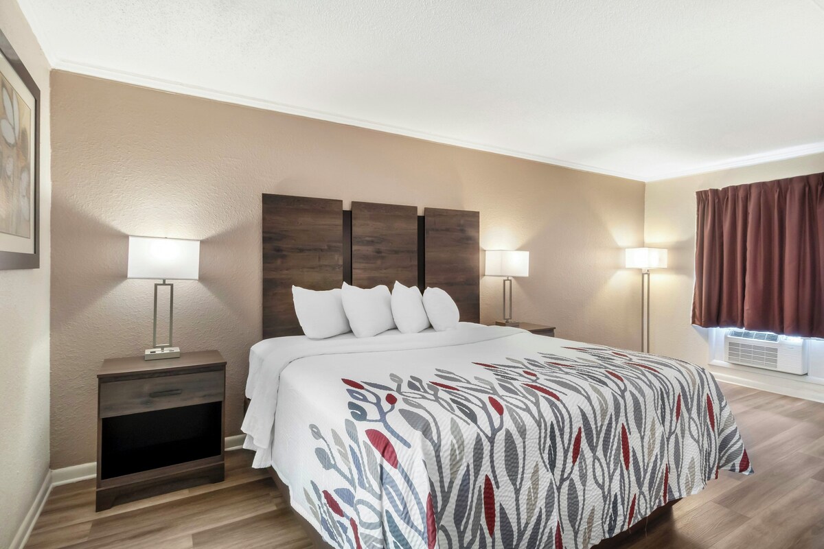 A hotel room with a bed, two bedside tables with lamps, a headboard, and a window with curtains.
