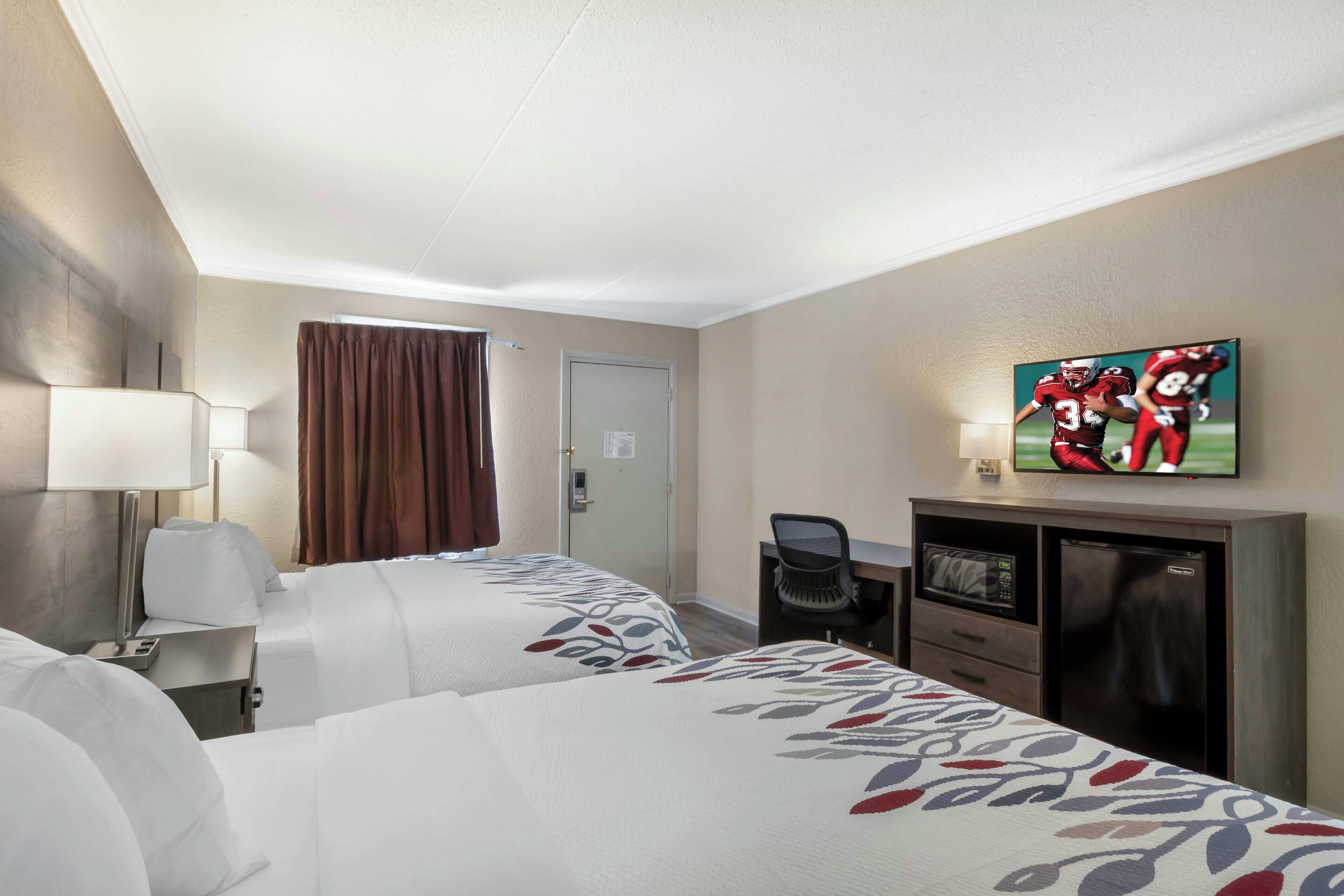 A hotel room with two beds, a desk, a television, and a door.