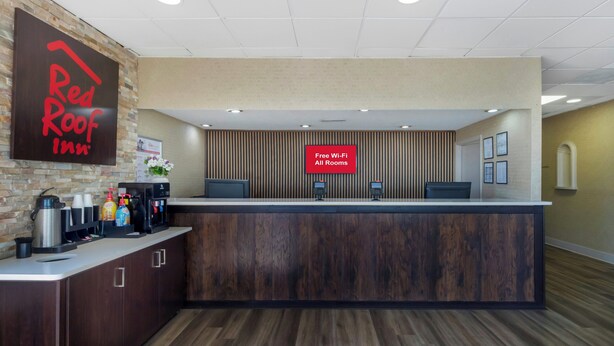 A Red Roof Inn reception desk with a 'Free Wi-Fi All Rooms' sign, a coffee station, and a brick wall backdrop. - Red Roof Inn Manchester, TN (Manchester)