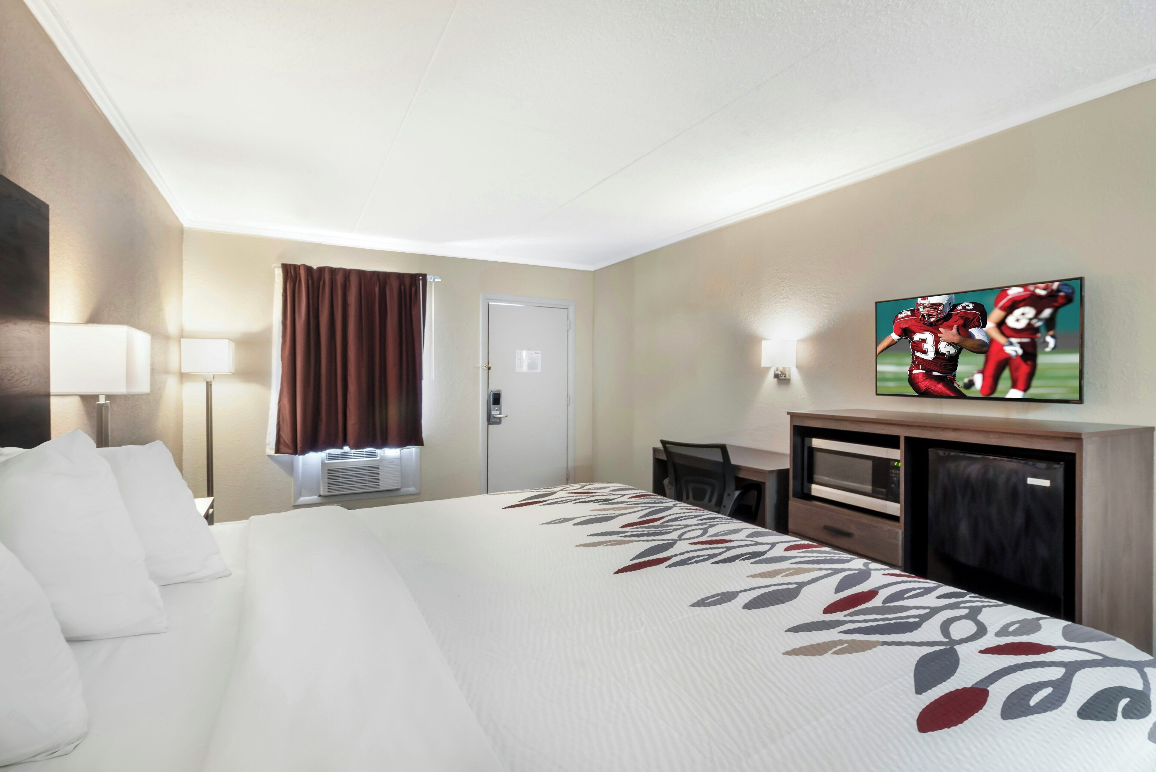 Une chambre d’hôtel avec un lit, un bureau, une télévision et une porte.