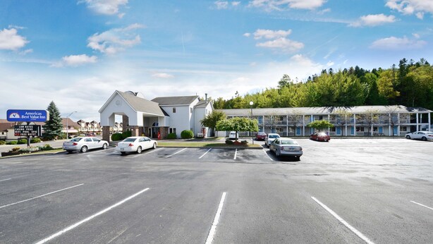 A parking lot with several cars, a motel with a sign for 'Americas Best Value Inn', and a building with a large glass facade in the background. - Americas Best Value Inn St. Ignace (St Ignace)