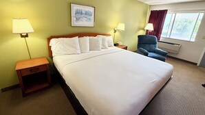A hotel room with a large bed, two bedside tables, a chair, a window with curtains, and a painting on the wall.