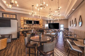 A modern restaurant with round tables, bar seating, and a large TV screen. - Delta Hotels by Marriott Detroit Novi (Farmington Hills)