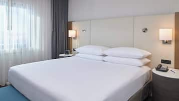 Ein Hotelzimmer mit einem großen Bett, einem Nachttisch mit Lampe, einem Telefon und einem Fenster mit Vorhängen.