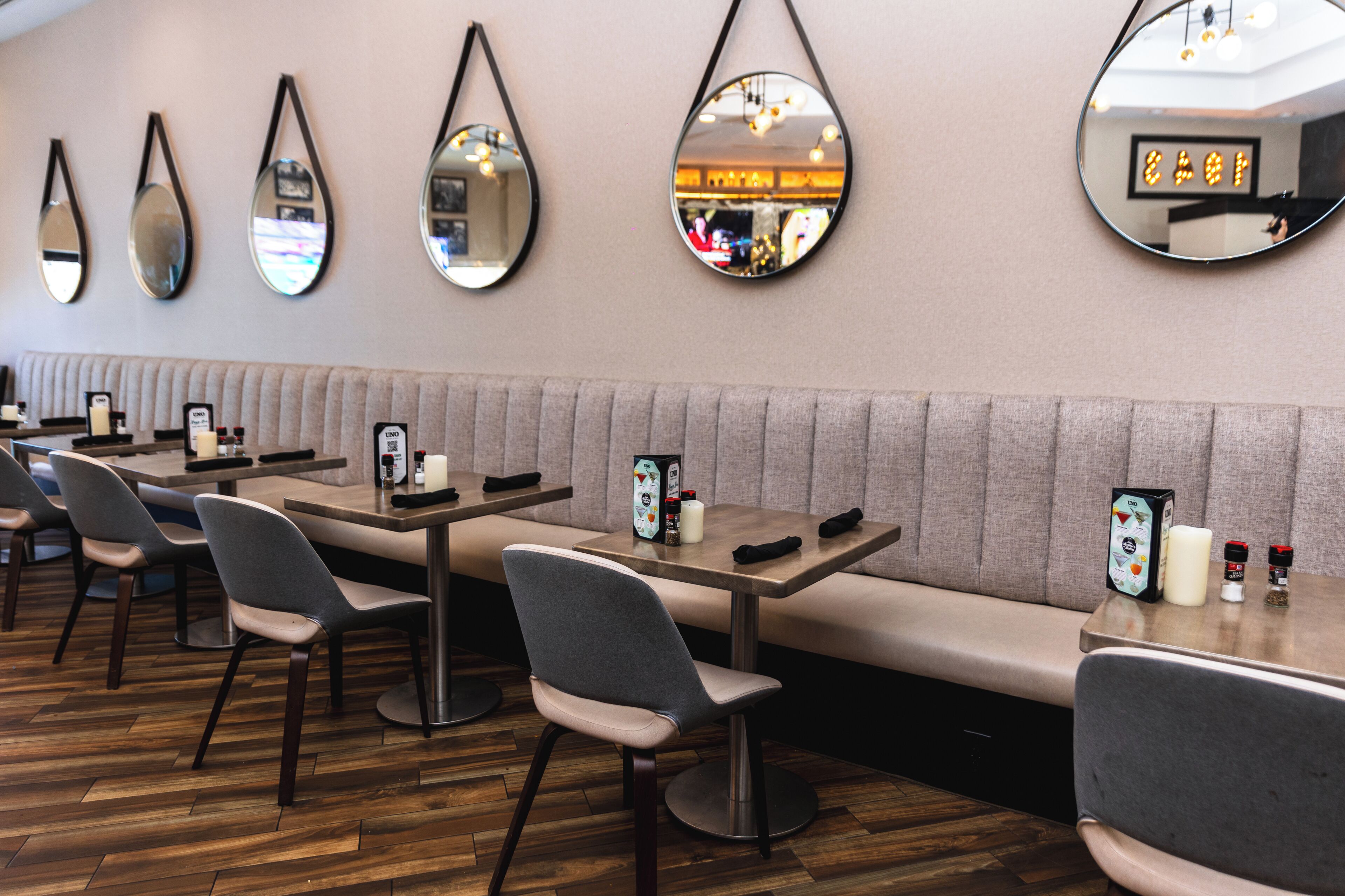 A restaurant with multiple tables and booths, a wooden floor, and wall-mounted mirrors.