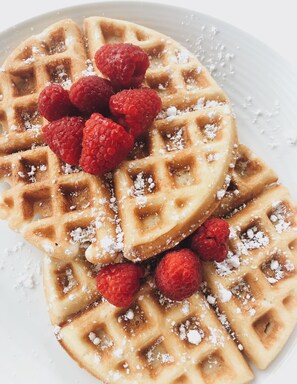 A plate of waffles with raspberries and powdered sugar.