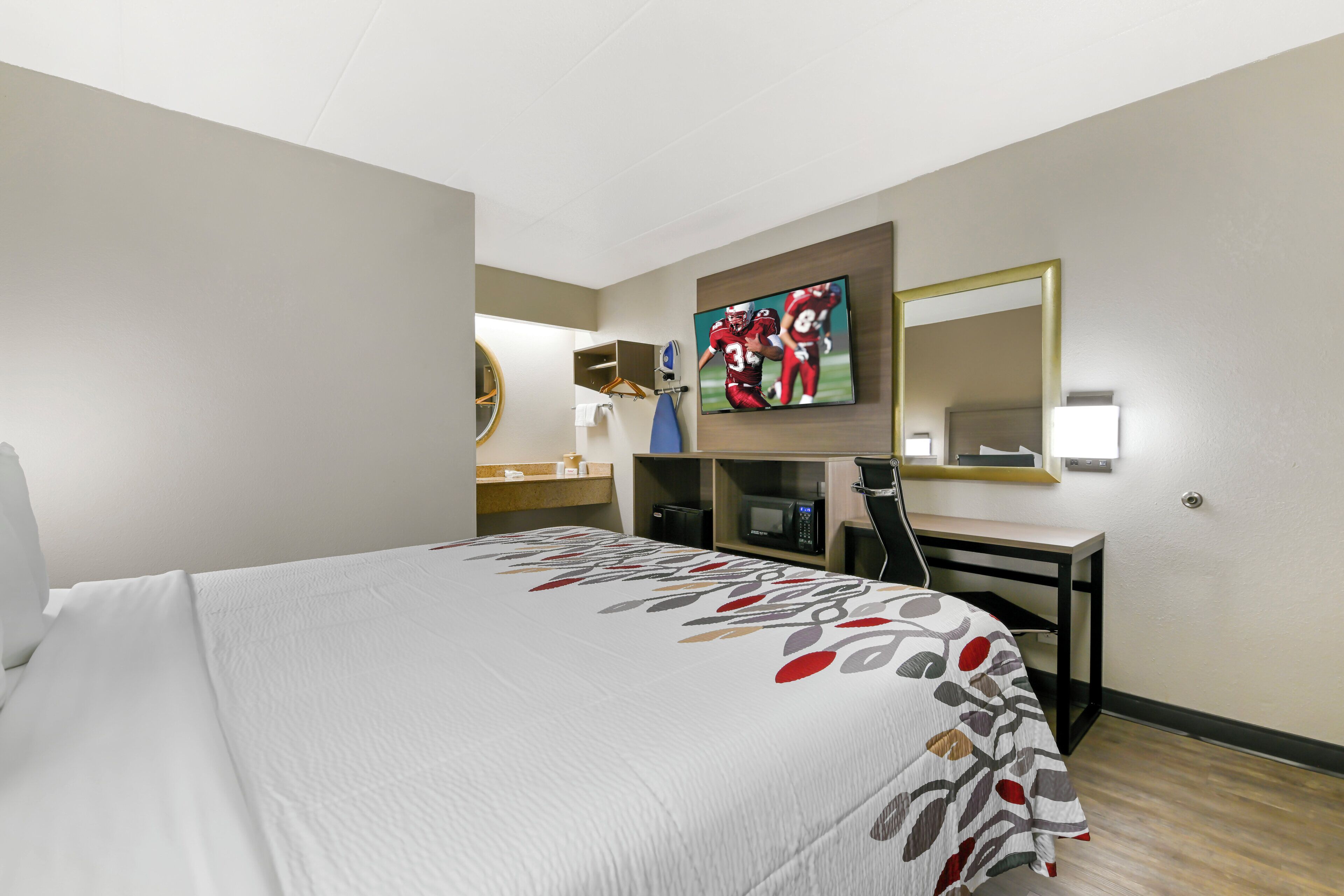 Habitación de hotel con cama, escritorio, televisor y espejo.