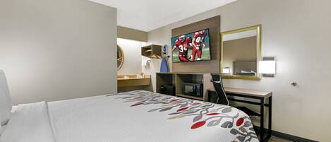 Habitación de hotel con cama, escritorio, televisor y espejo.
