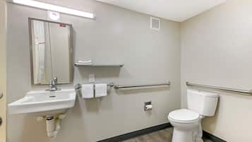 A bathroom with a sink, mirror, towel rack, toilet, and handrail.