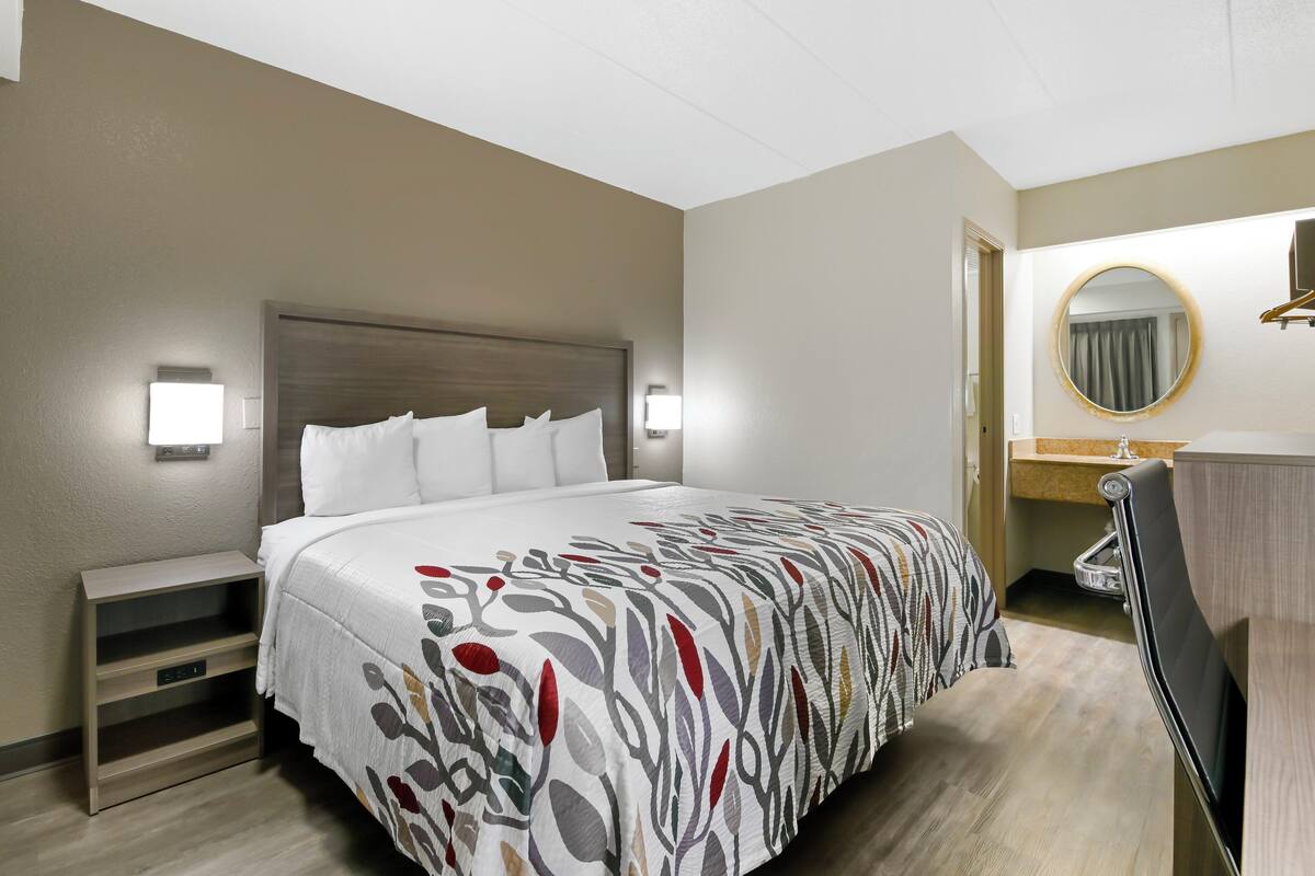 A hotel room with a large bed, bedside tables, a mirror, and a wooden dresser.