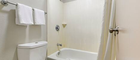 Une salle de bain équipée de toilettes, d’une baignoire et d’une douche. Des serviettes sont suspendues à un porte-serviettes.