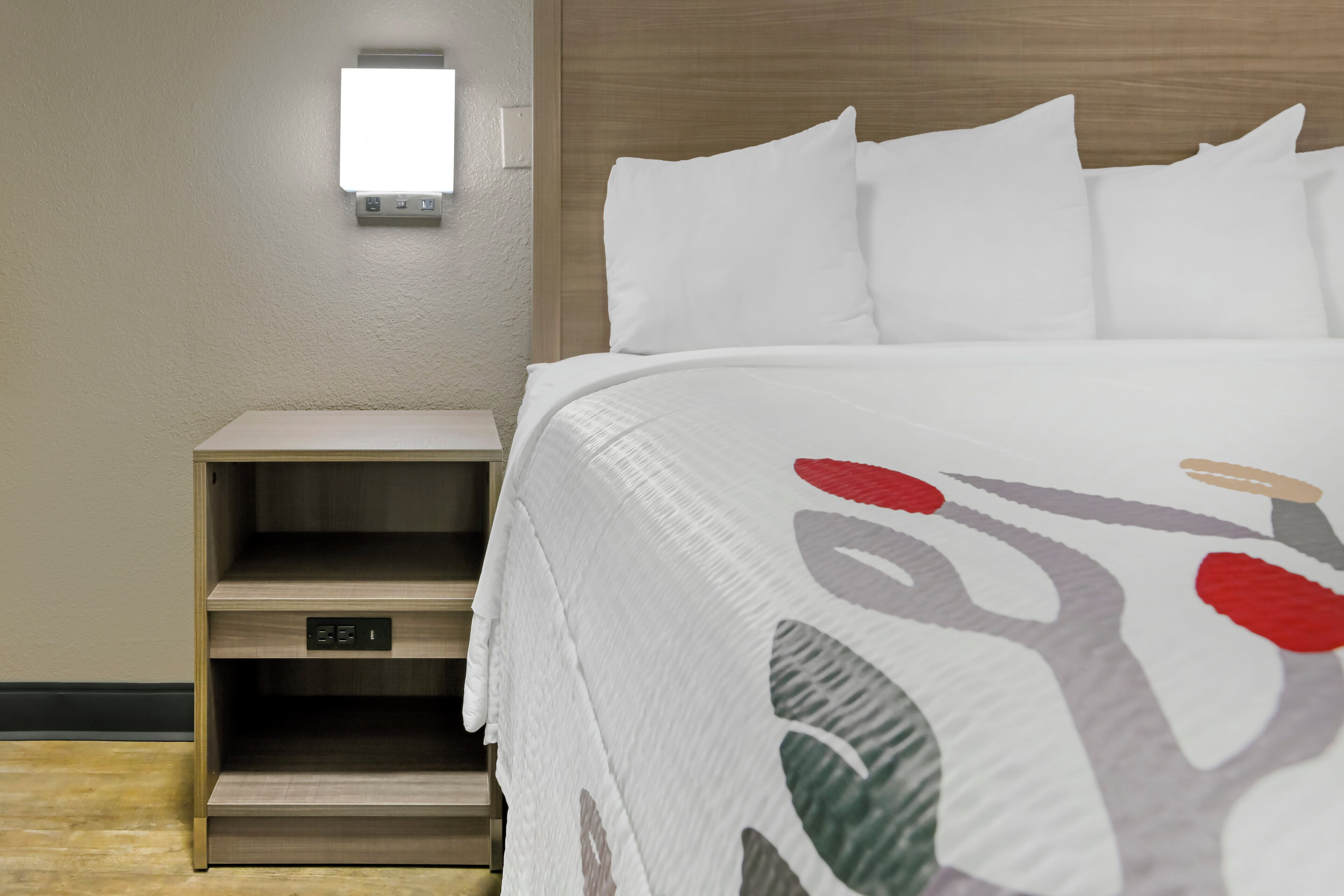 Quarto de hotel com cama, mesa de cabeceira e luminária na parede.