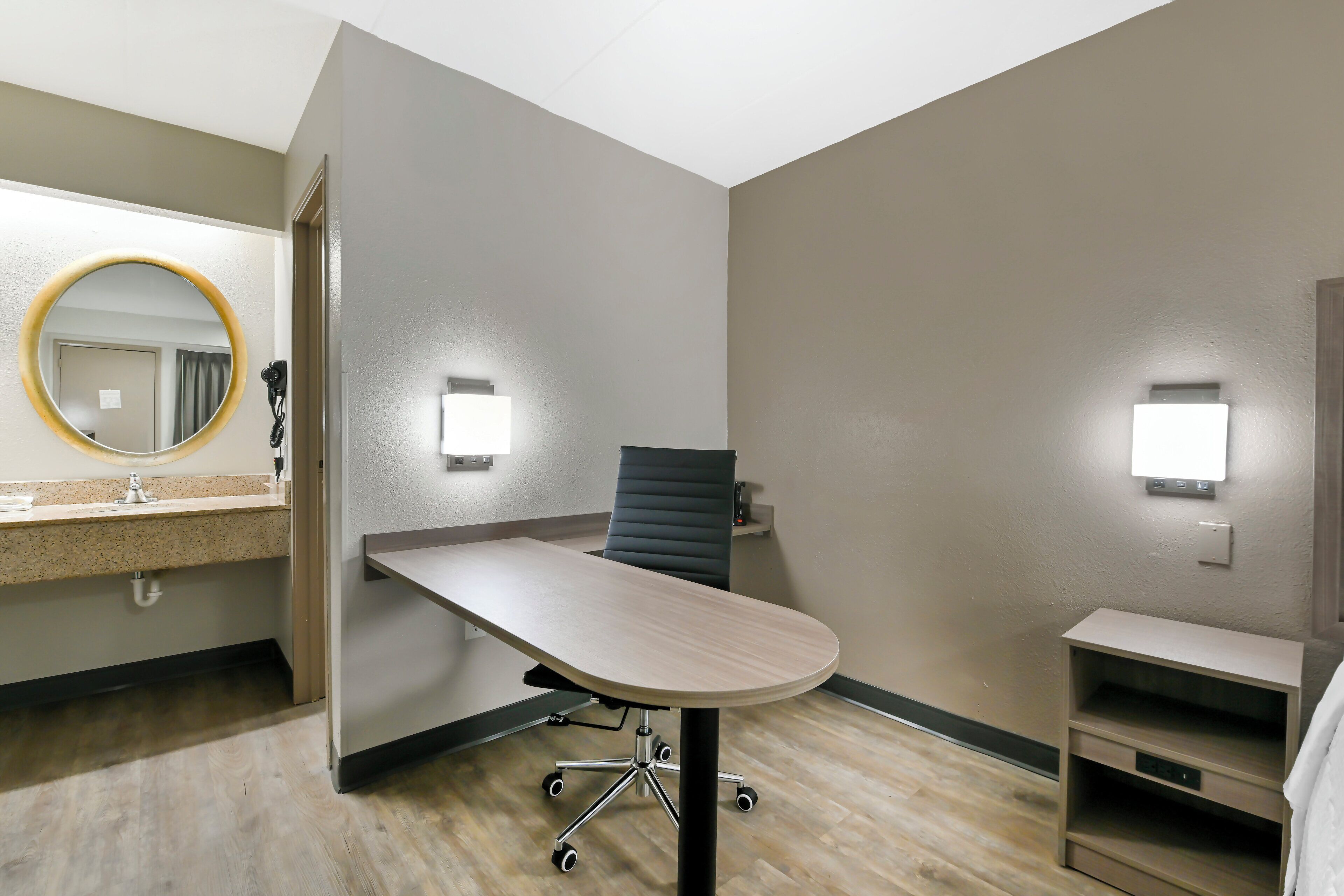 A hotel room with a desk, chair, and a mirror.