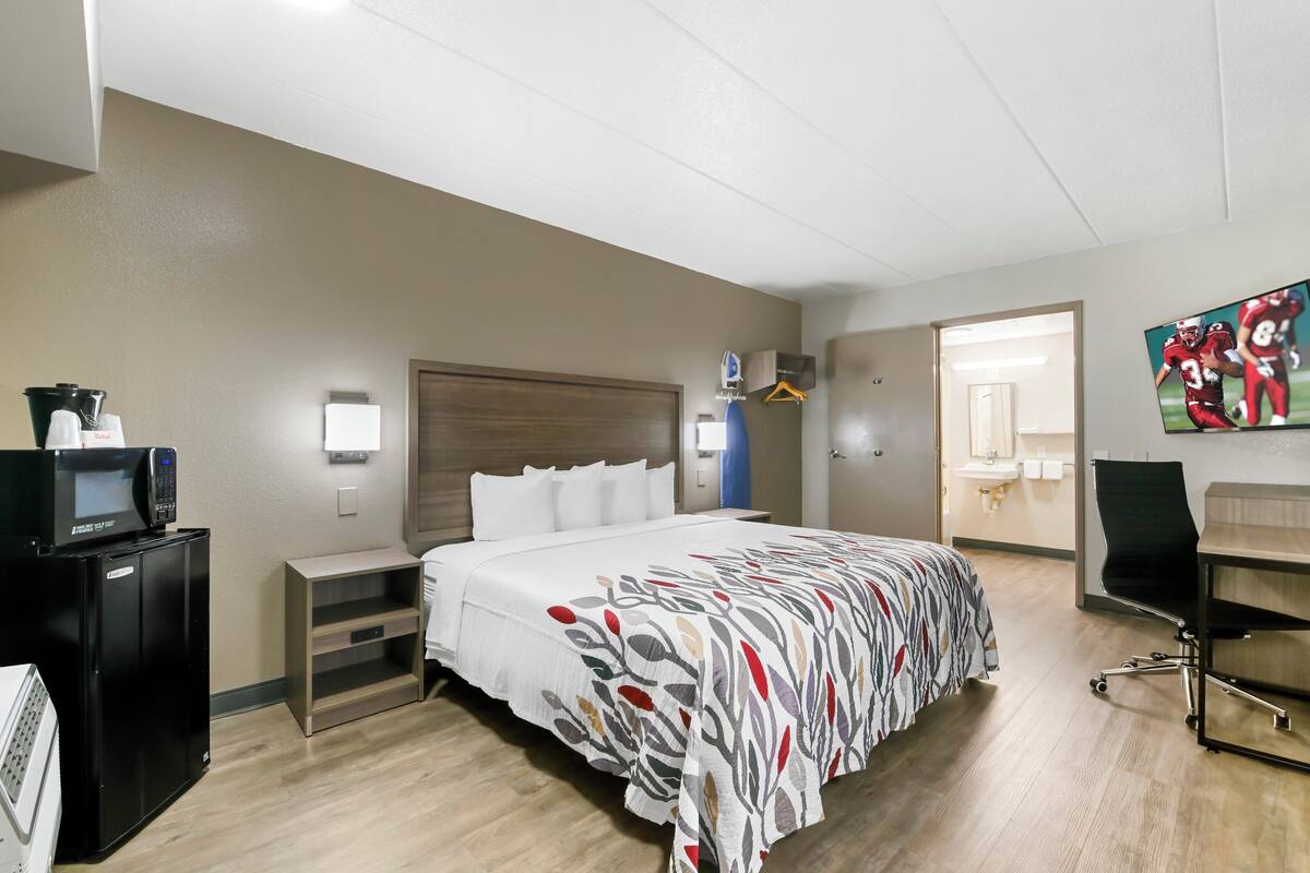 A hotel room with a bed, a desk, a chair, a microwave, and a TV.