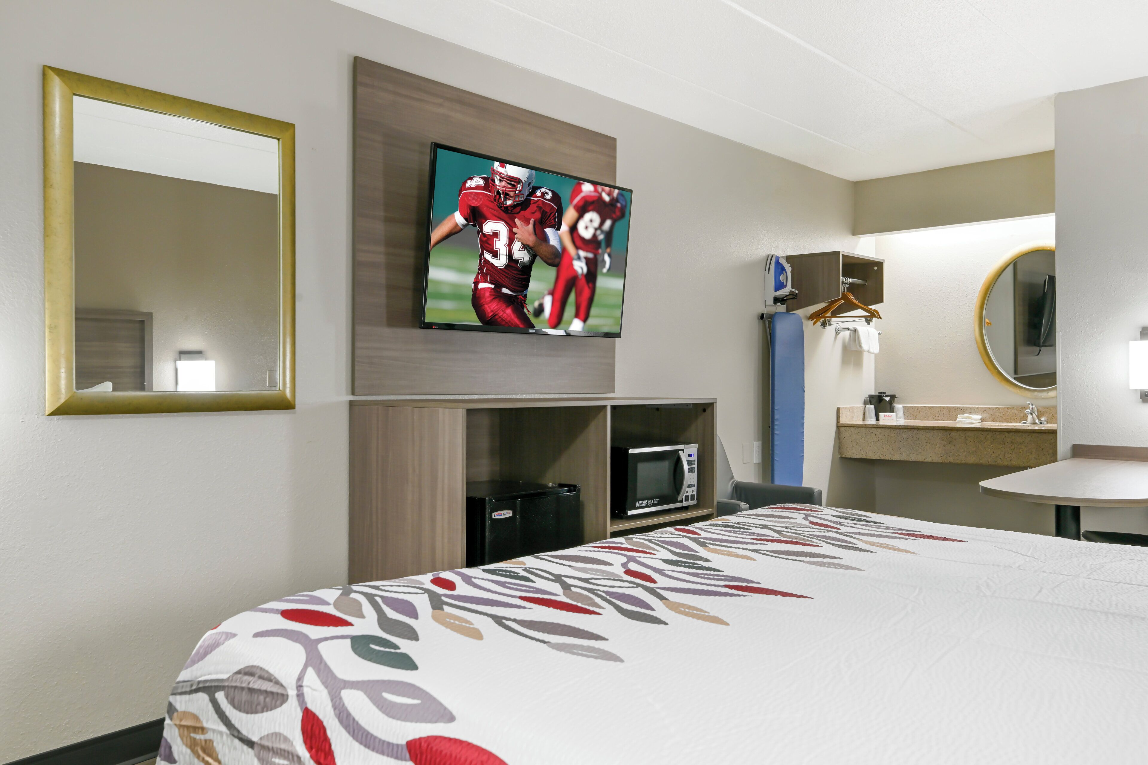 A hotel room with a bed, a television mounted on the wall, a microwave, and a small refrigerator.