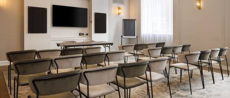 Un salón de conferencias con una mesa larga y varias sillas, un televisor de pantalla plana y una pizarra.