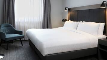 A neatly made bed with white linens, a dark headboard, and a bedside lamp.