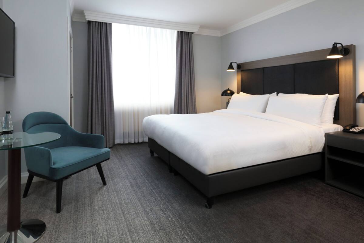 Une chambre d’hôtel avec un grand lit, une chaise, une table de chevet avec une lampe et un téléviseur fixé au mur.
