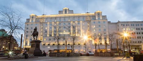 Un edificio grande e histórico con una estatua en primer plano, probablemente un hotel o edificio público.
