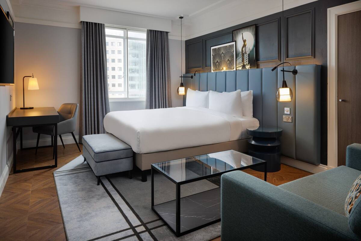 Une chambre d’hôtel avec un grand lit, un bureau, une chaise, une table basse en verre et un canapé.