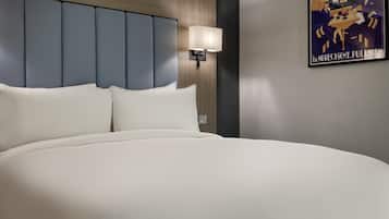 A large bed with a headboard, a wall-mounted lamp, and a poster on the wall.