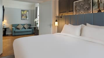A modern hotel room with a large bed, a blue sofa, and a small table with a lamp.