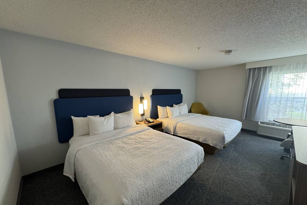 A hotel room with two beds, a desk, and a chair.
