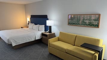 Ett hotellrum med en säng, en soffa, ett nattduksbord, en lampa och en tavla på väggen.
