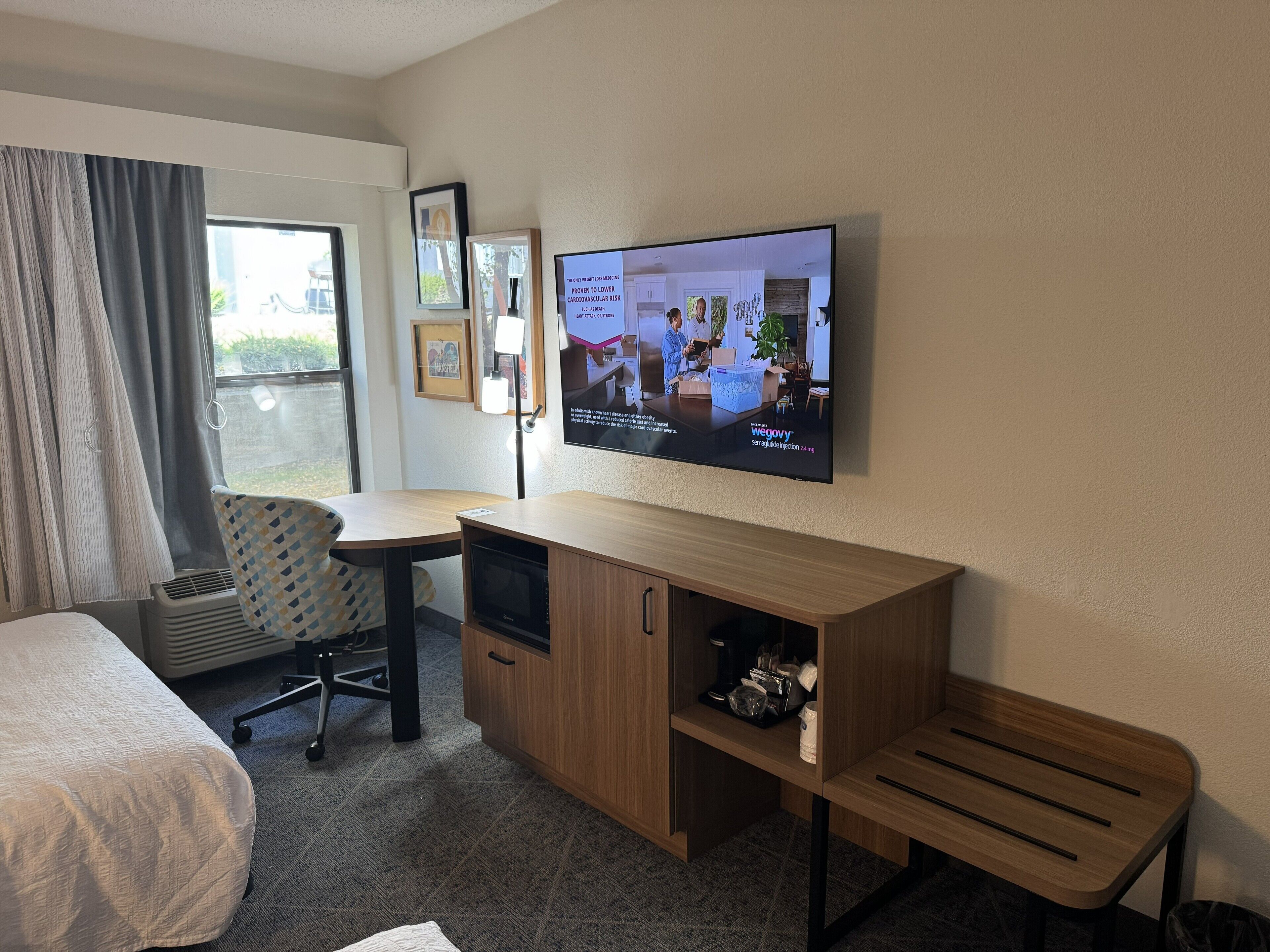 A hotel room with a bed, a desk, a chair, a television, and a window with curtains.