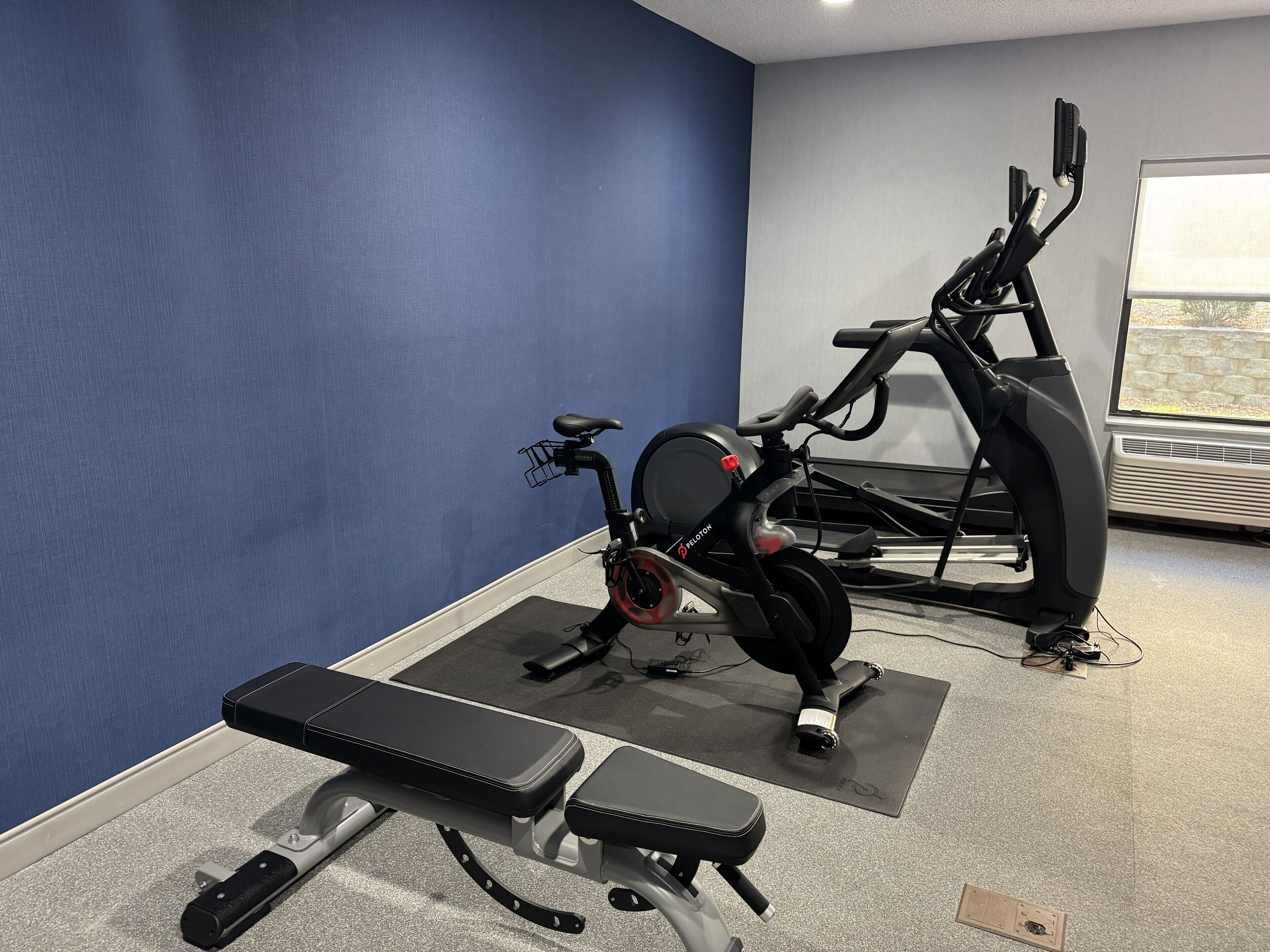 Une salle de sport équipée d’un vélo d’appartement, d’un tapis de course et d’un banc de musculation.