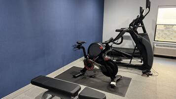 Une salle de sport équipée d’un vélo d’appartement, d’un tapis de course et d’un banc de musculation.