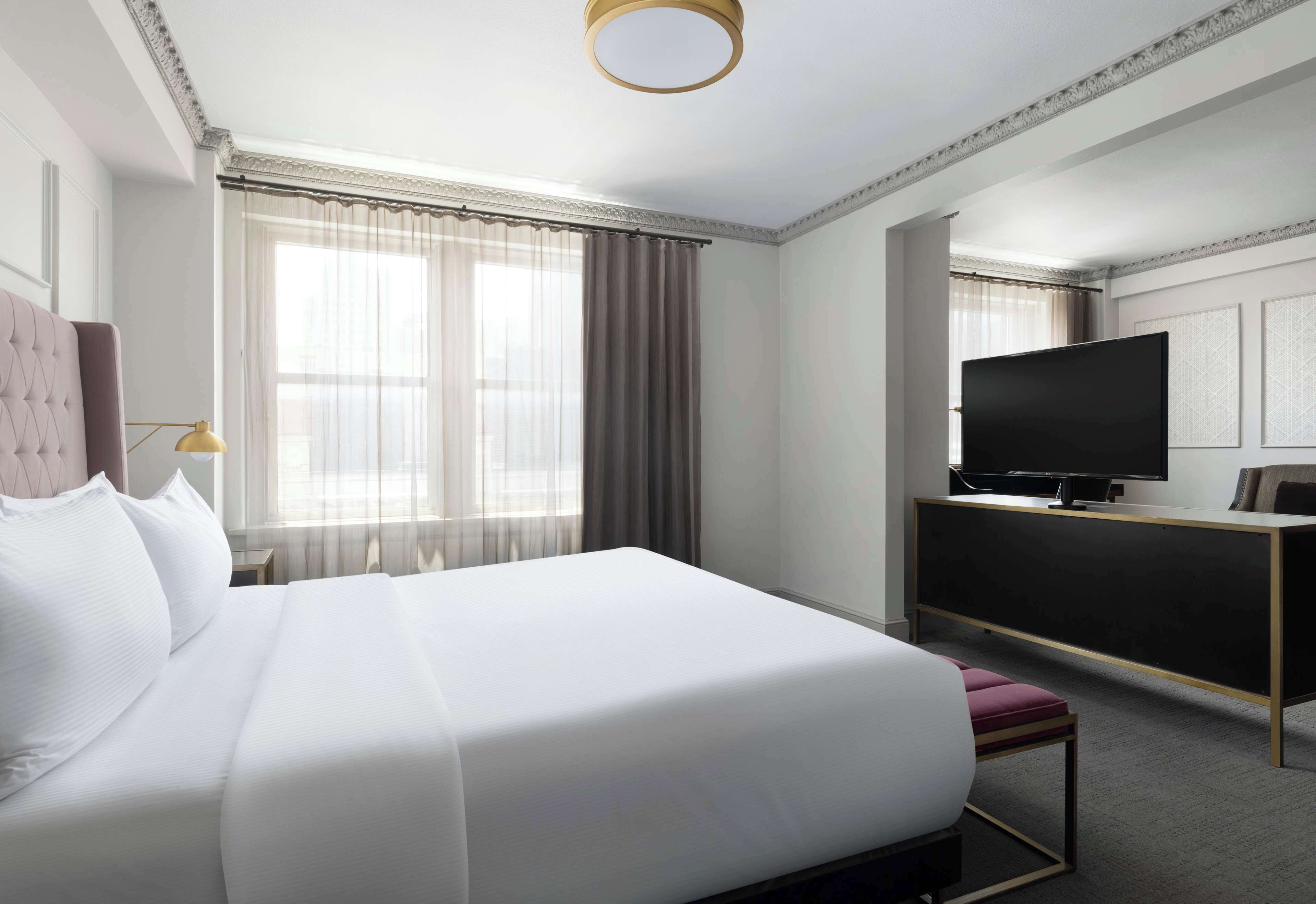 Ein Hotelzimmer mit einem großen Bett, einem Fernseher auf einem Schreibtisch und einem Fenster mit Vorhängen.